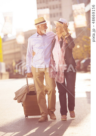 Happy cheerful senior couple of tourists with map and city guide walking on street Happy cheerful senior couple of tourists with map and city guide walking on street 48669156