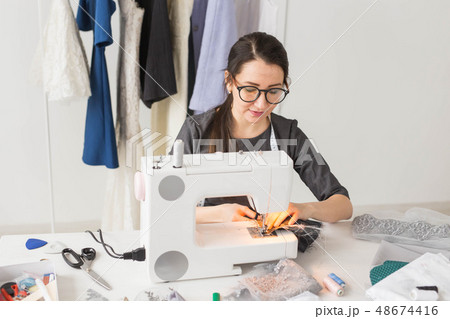 people, fashion and showroom concept - young fashion designer sews clothes on a sewing machine people, fashion and showroom concept - young fashion designer sews clothes on a sewing machine 48674416