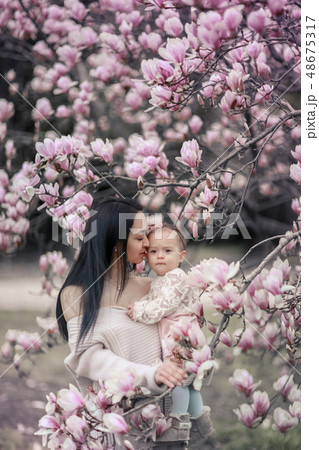 Cute Baby 6 month old Girl in Pink Outfit with Big Blue Eyes with Young Beautiful Mother at Spring 48675317