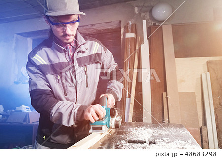 Young carpenter with a beard working with an electric plane with suction of sawdust. Leveling and 48683298