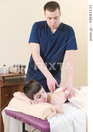 A little boy relaxes from a therapeutic massage. Male massage therapist makes a medical massage to A little boy relaxes from a therapeutic massage. Male massage therapist makes a medical massage to 48683531