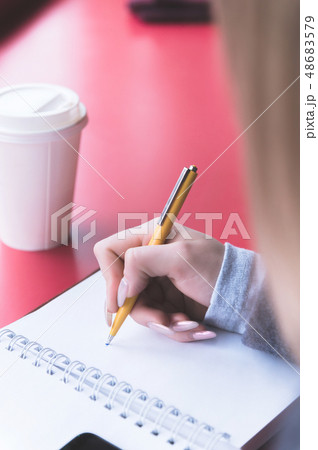 Close-up from behind the back of a young woman in a winter polto is holding a ballpoint pen and is 48683579