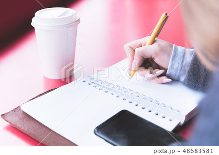 Close-up from behind the back of a young woman in a winter polto is holding a ballpoint pen and is 48683581