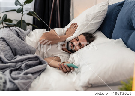 Sleepy brunette man lying with a pillow on his ear Sleepy brunette man lying with a pillow on his ear 48683619
