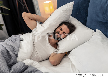 Unhappy cheerless young man covering his ears Unhappy cheerless young man covering his ears 48683646