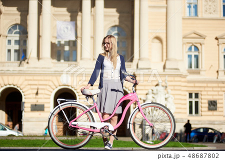 Young attractive blond woman in glasses with pink lady bicycle on city street on sunny summer day. 48687802