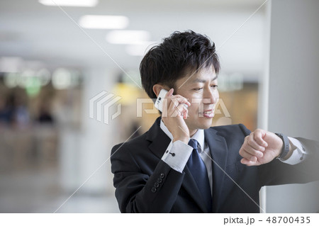 空港で腕時計を見ながら通話するビジネスマン 空港で腕時計を見ながら通話するビジネスマン 48700435