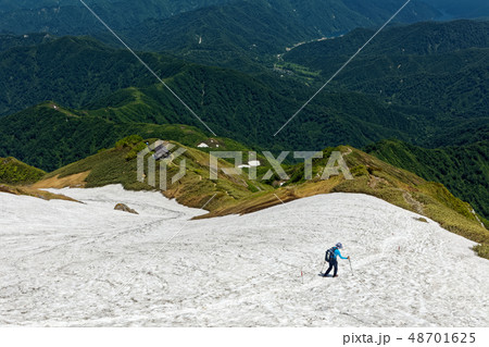 越後駒ヶ岳山頂直下の雪渓を行く登山者と銀山平方面の眺め 48701625