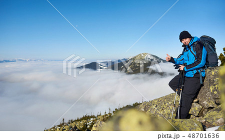 Hiker man on rocky hill on foggy valley with white clouds, snowy mountains and blue sky background. Hiker man on rocky hill on foggy valley with white clouds, snowy mountains and blue sky background. 48701636