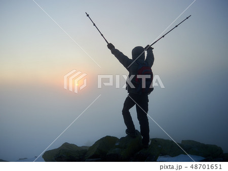 Tourist hiker man with backpack on rocky mountain on misty blue sky and raising sun background. 48701651