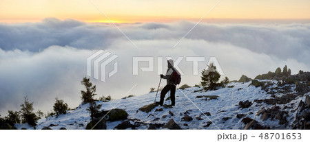 Tourist with backpack hiking on rocky mountain peak on background of foggy valley and blue sky at 48701653