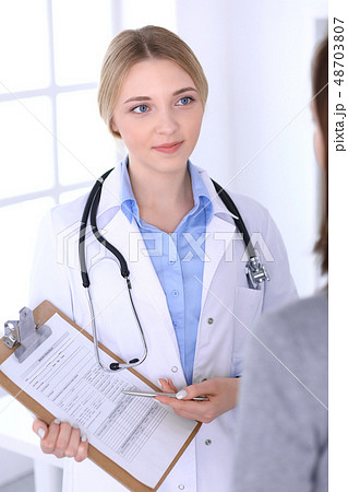 Young woman doctor and patient looking at medication history records while standing straight in Young woman doctor and patient looking at medication history records while standing straight in 48703807