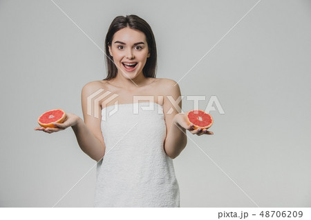 Happy young girl posing with fruit. Slices of red grapefruit in her hands on a white background 48706209