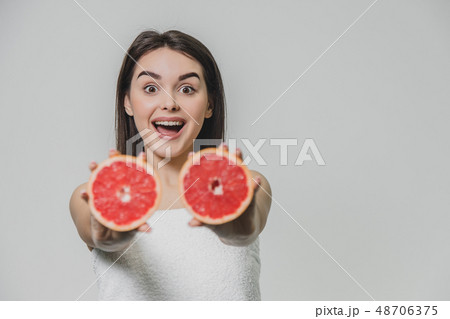Young sexy girl posing with slices of red grapefruit in her arms extended forward. On a gray Young sexy girl posing with slices of red grapefruit in her arms extended forward. On a gray 48706375