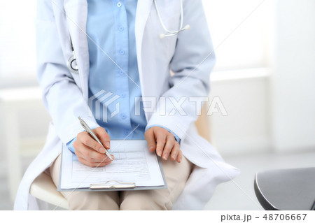 Female doctor writing up medication history records form on clipboard, while sitting at the chair 48706667