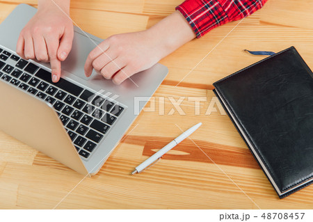 Workspace with laptop, women's hands, gray notebook, white pen and black pad on the table. Flat 48708457