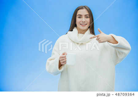 Interestingly, a young woman in a knitted white sweater. Holds a white cup of coffee or tea in his Interestingly, a young woman in a knitted white sweater. Holds a white cup of coffee or tea in his 48709364