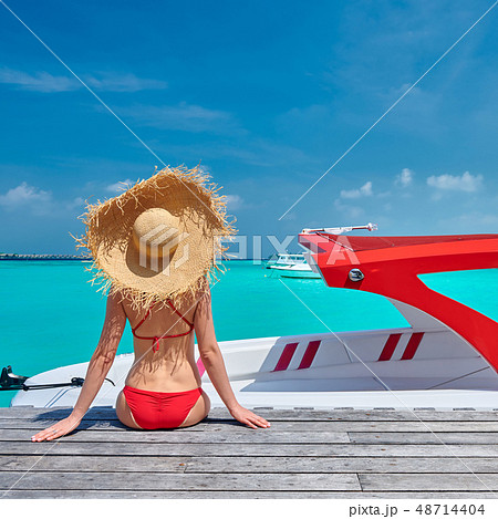 Woman in bikini sitting on jetty with boat Woman in bikini sitting on jetty with boat 48714404