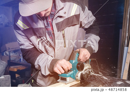 A young carpenter with a beard works with an electric plane without suctioning sawdust. Leveling and 48714858