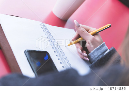 Close-up from behind the back of a young woman in a winter polto is holding a ballpoint pen and is 48714886