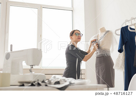 Dressmaker, tailor, fashion and showroom concept - Side view of female fashion designer measuring Dressmaker, tailor, fashion and showroom concept - Side view of female fashion designer measuring 48716127