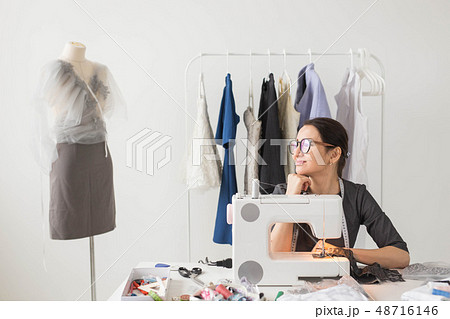 Dressmaker, tailor and fashion concept - Smiling female fashion designer using sewing machine and 48716146