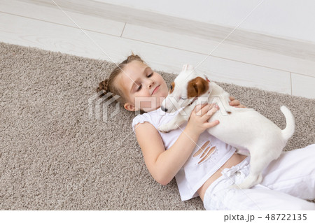 Pet, childhood and animal concept - Portrait of little child girl lying on the floor with puppy Jack Pet, childhood and animal concept - Portrait of little child girl lying on the floor with puppy Jack 48722135