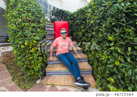 Travel, holiday and people concept - Happy handsome man tourist sitting on stairs with suitcase and 48725564