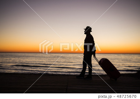 Relax man with suitcase on a beach at sunset silhouette. Holiday travel concept. Guy with suitcase 48725670