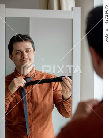 Candid view on young man dressing up near mirror  48729675