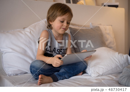 5 year old boy lying In bed playing game on tablet in bedroom,Education school technology internet 5 year old boy lying In bed playing game on tablet in bedroom,Education school technology internet 48730417