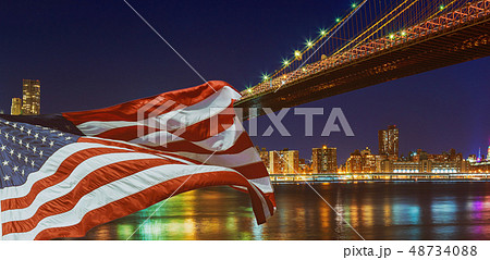 Brooklyn Bridge closeup over East River at night in New York City Manhattan and American flag flying Brooklyn Bridge closeup over East River at night in New York City Manhattan and American flag flying 48734088
