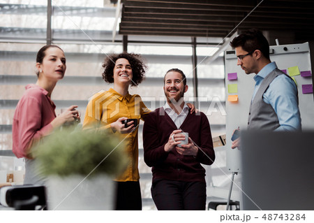 A group of young businesspeople with cup of coffee standing in office, talking. 48743284