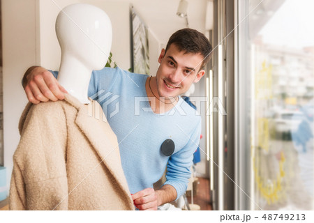 Young man putting clothes on a mannequin in store. 48749213