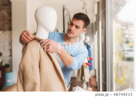 Man putting clothes on a mannequ in store. 48749215
