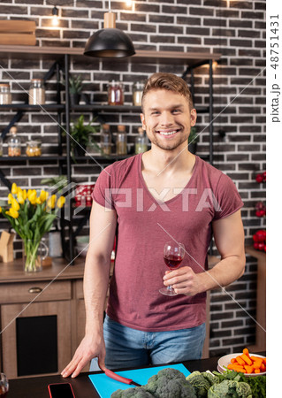 Beaming husband cooking dinner with vegetables and drinking wine 48751431