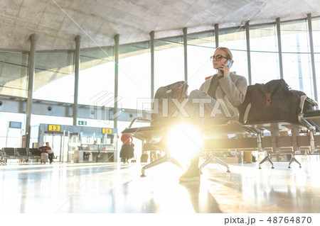 Female traveler talking on her cell phone while waiting to board a plane at departure gates at Female traveler talking on her cell phone while waiting to board a plane at departure gates at 48764870