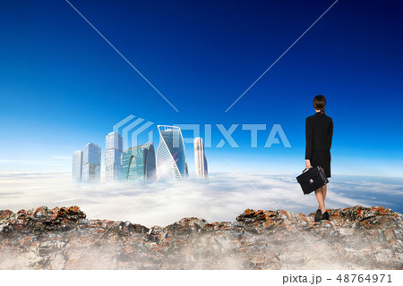 Business woman stands on the edge of mountain and looking on city. 48764971