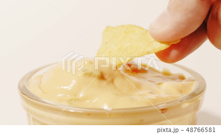 Man dips tortilla chip into cheese sauce, close-up shot 48766581