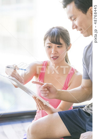 パーソナルジムで美女インストラクターから筋トレーニングの説明を受ける若い男性会社員細マッチョ 48768445