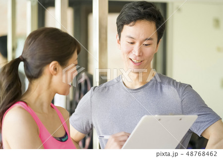 パーソナルジムで美女インストラクターから筋トレーニングの説明を受ける若い男性会社員細マッチョ 48768462