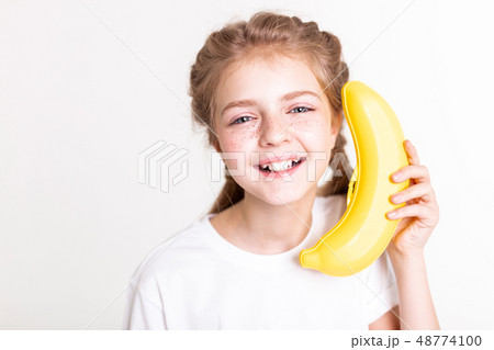 Laughing light-haired young girl holding plastic banana near her ear 48774100