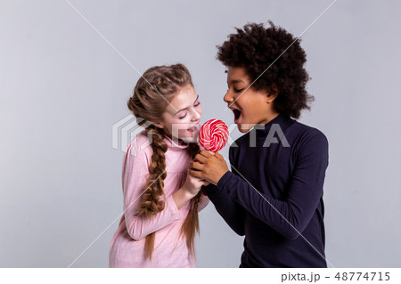 Active beaming opposite kids biting one candy together 48774715