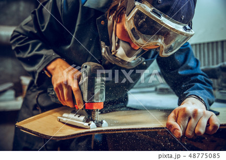 Carpenter using circular saw for cutting wooden boards. 48775085