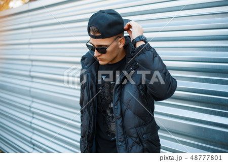 Young man in black stylish dress near metal wall. 48777801