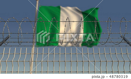 Defocused waving flag of Nigeria behind barbed wire fence. 3D rendering 48780319