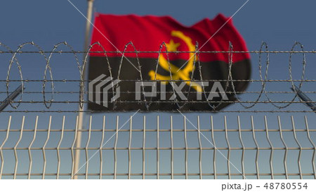 Blurred waving flag of Angola behind barbed wire fence. 3D rendering Blurred waving flag of Angola behind barbed wire fence. 3D rendering 48780554