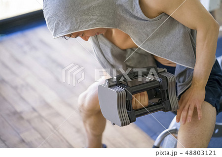 可変式ダンベルで腕の筋肉上腕三頭筋を鍛えるパーカーを着た真剣な表情の若い男性 48803121