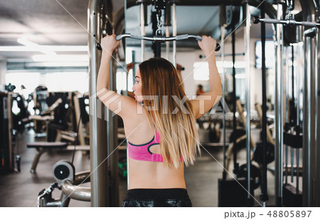 A rear view of young girl or woman doing strength workout in a gym. A rear view of young girl or woman doing strength workout in a gym. 48805897