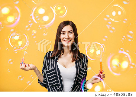Young woman blows soap bubble, yellow background Young woman blows soap bubble, yellow background 48808588